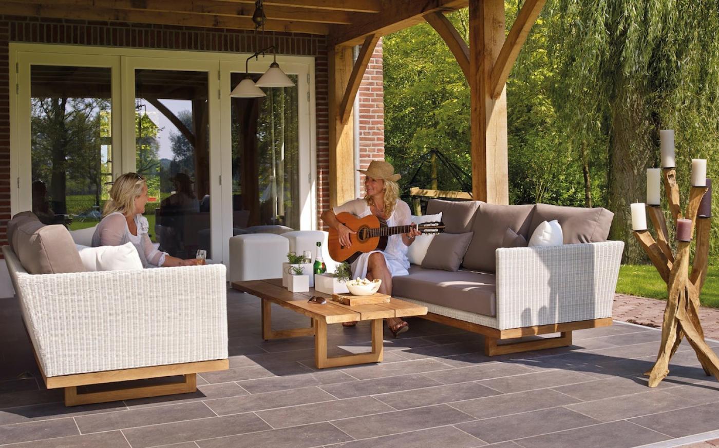 Two women sitting outside on a patio. One woman is playing guitar, and the other is listening and smiling.