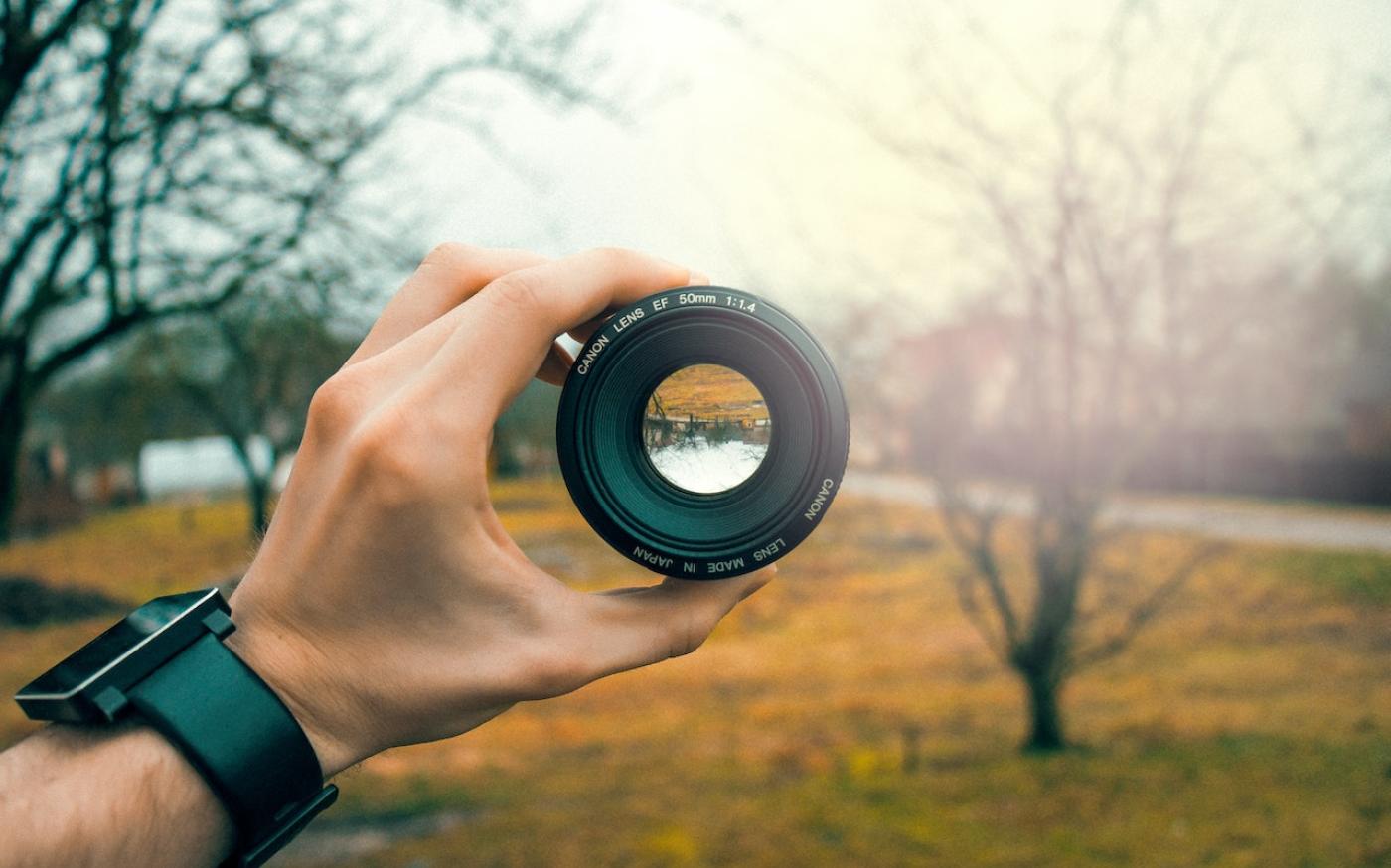 Person holding a camera lens in a field. The view of the field within the camera lens is upside down.