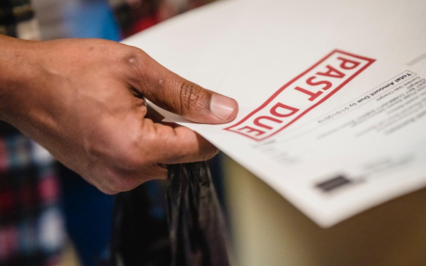 Hand holding a bill with a red "Past Due" stamp on it