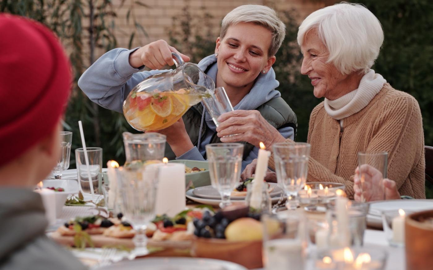 Young woman pouring a drink for an older woman. They are sitting together at a table.